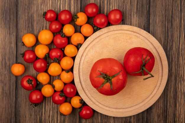 Free photo top view of fresh red tomatoes on a wooden kitchen board with cherry tomatoes isolated on a wooden wall
