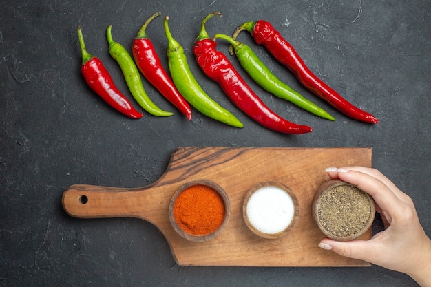 Free Photo top view horizontal row green and red peppers different spices on cutting board female hand on dark surface