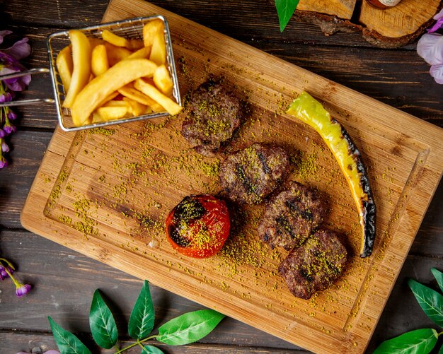 Top view of lamb steak pieces served with french fries grilled pepper and tomato