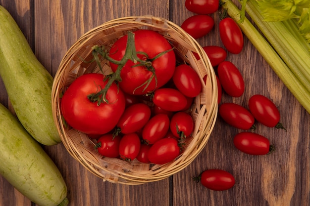 Free photo top view of organic red tomatoes on a bucket with zucchinis and celery isolated on a wooden wall