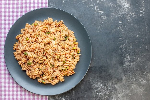 Foto gratuita pasta rotini vista dall'alto su piatto rotondo su tovaglia a quadretti rosa bianca su superficie scura con spazio libero