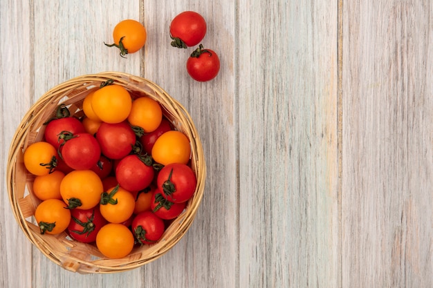 Free photo top view of rounded red and orange tomatoes on a bucket on a grey wooden wall with copy space