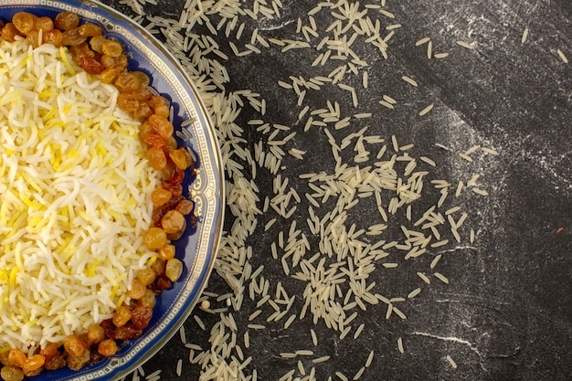 Foto gratuita una vista dall'alto gustoso pilaf con olio e uvetta essiccata all'interno del piatto con riso crudo sulla superficie scura