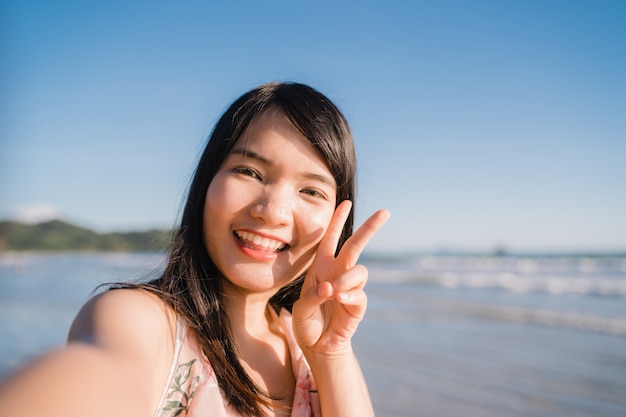 Free photo tourist asian woman selfie on beach, young beautiful female happy smiling using mobile phone taking selfie