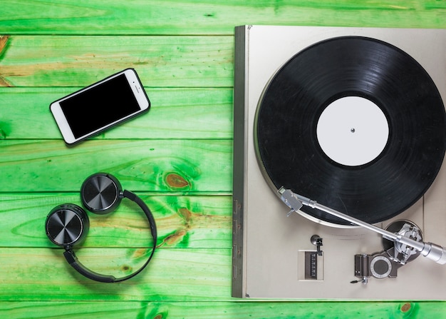 Free photo turntable vinyl record player; headphone and cellphone on green wooden backdrop