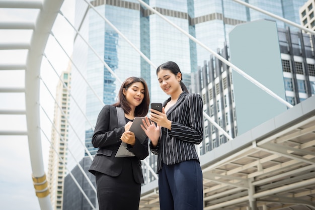 Free photo two business woman standing using smartphone and discussing in front of the office. business working concept.