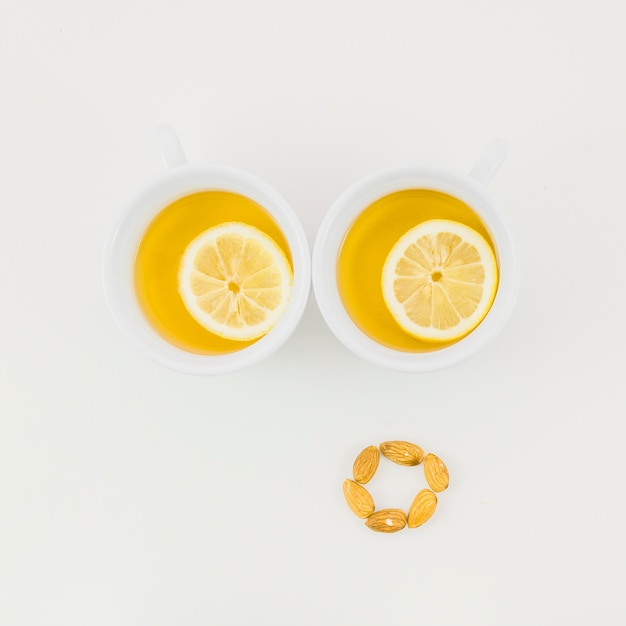 Two cup of ginger tea with lemon slice and almonds isolated on white backdrop