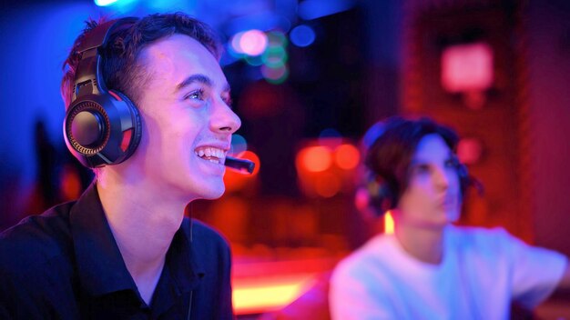 Two teen friends in headphones are playing a game console using gamepads and smiling