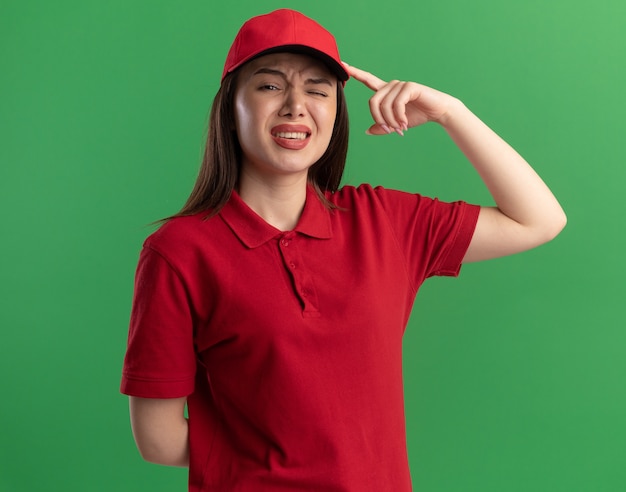 Free photo unpleased pretty delivery woman in uniform puts finger on head on green