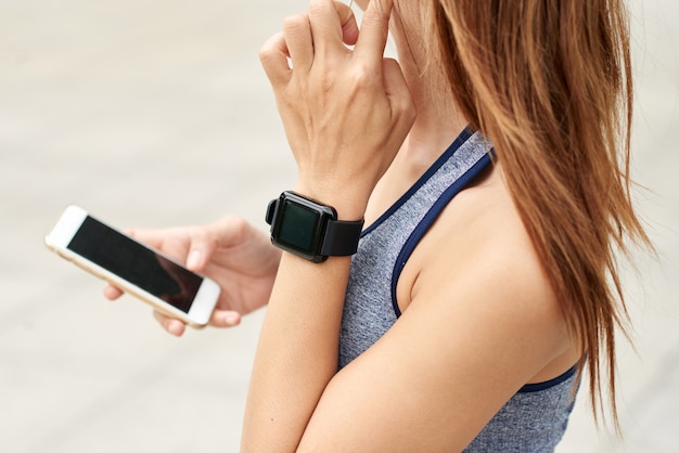 Unrecognizable athletic woman with smart watch checking pulse and using smartphone