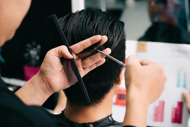 Unrecognizable hairdresser cutting customer's hair with comb and scissors in salon