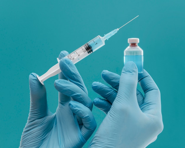 Free Photo vaccine bottle and syringe held by doctor with gloves