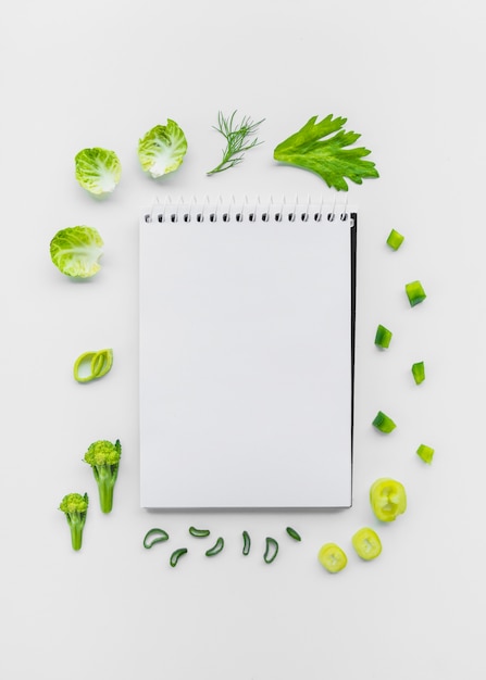 Varieties of chopped vegetables surrounding spiral notepad on white backdrop