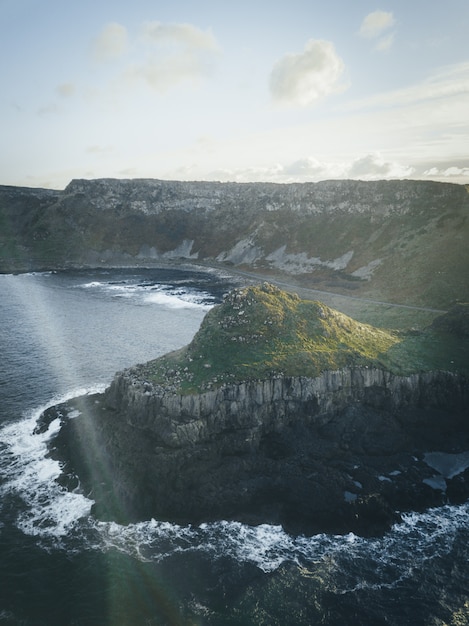 Vertical shot of a cliff by the water under a clear sky with clouds