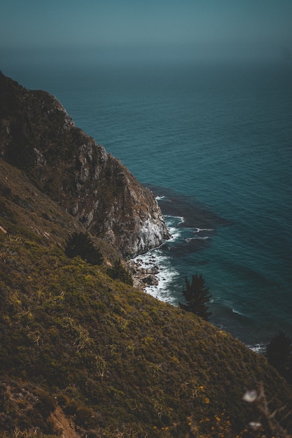 Vertical shot of a hilly green coast and blue ocean with rocks