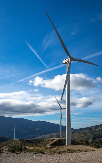 Vertical shot of several white electric windmills on a hill