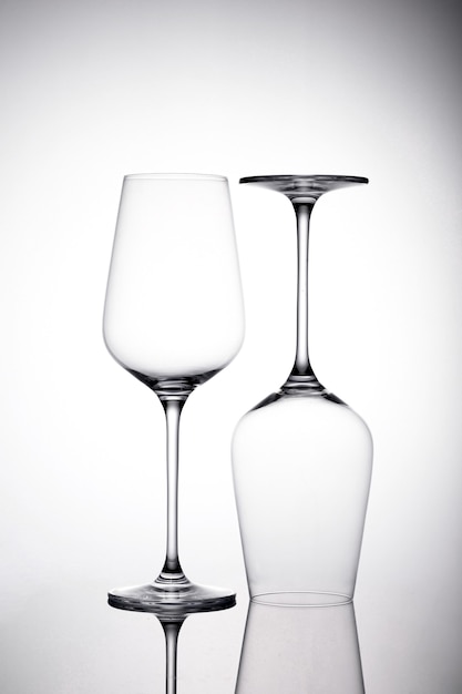 Free photo vertical shot of two empty wineglasses on the white surface with shadows, one is upside down