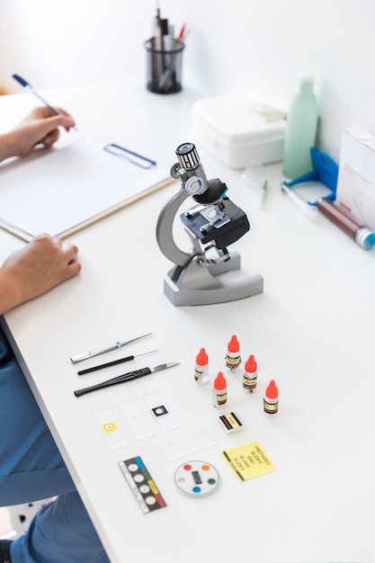 Free photo veterinarian writing on clipboard with microscope and medical equipments in laboratory desk