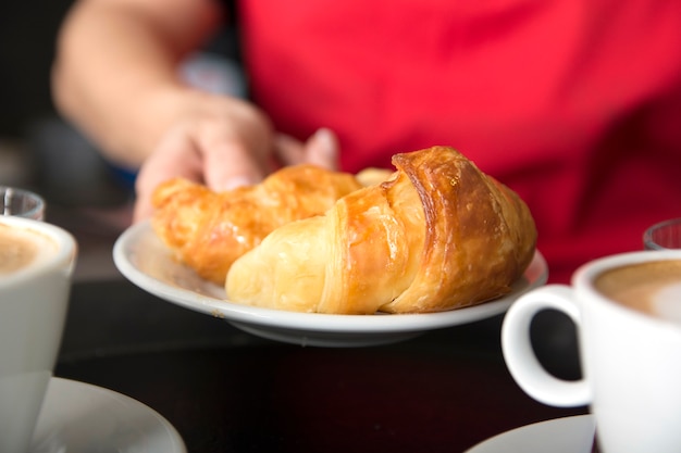 Foto gratuita la mano della cameriera che offre il croissant al forno fresco in piatto