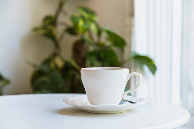 Foto gratuita tazza e cucchiaio di caffè macchiato sul piattino ceramico sopra la tavola bianca