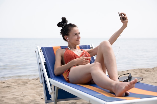 Free Photo woman on beach chair taking a selfie