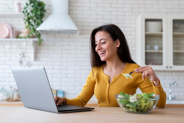 Woman checking laptop and eating salad