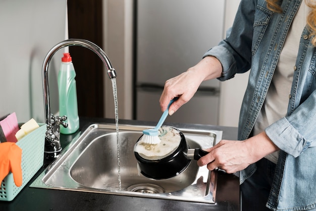 Free photo woman cleaning a pot in the sink with brush