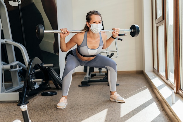 Free photo woman exercising at the gym with equipment and medical mask