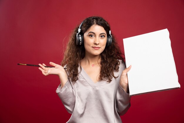 Woman in headphones posing with brush and canvas.