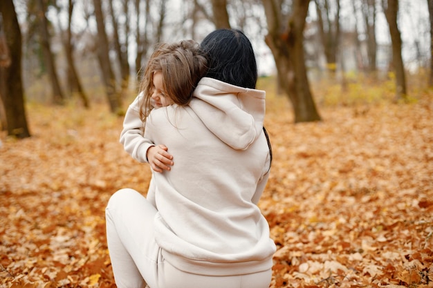 Free photo woman and her little girl playing in autumn forest and laughing brunette man hugging her daughter family wearing beige sportive costumes