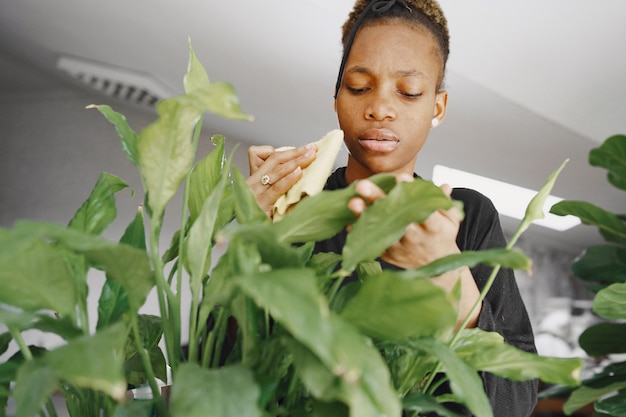 Free photo woman at home. girl in a black sweater. african woman use the rag. person with flowerpot.