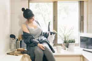 Free photo woman sitting in kitchen with her cat