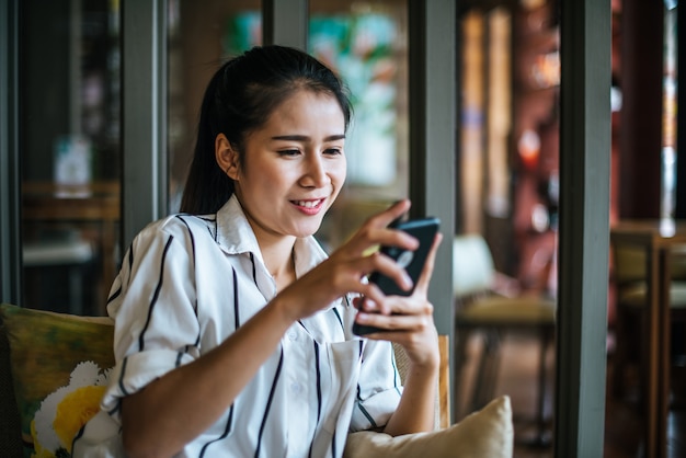 Free photo woman sitting and playing her smart phone at cafe