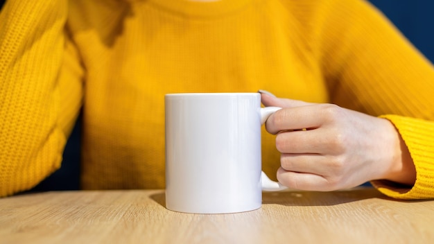 Free Photo woman in sweater holding a cup on a wooden table