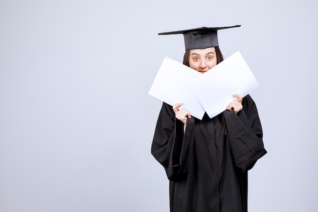 Free photo woman wearing graduation cap and ceremony robe showing empty papers. high quality photo