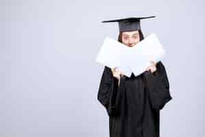 Free photo woman wearing graduation cap and ceremony robe showing empty papers. high quality photo