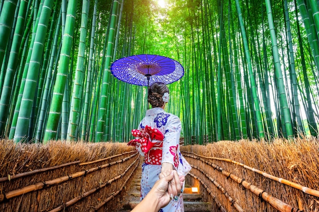 Free photo woman wearing japanese traditional kimono holding man's hand and leading him to bamboo forest in kyoto, japan.