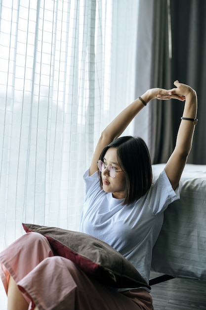 Free photo a woman in a white shirt sitting on the bed and raising both arms.