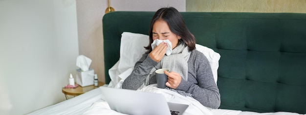 Free Photo woman with cold having flu staying in bed sneezing in napkin runny nose and influenza symptoms