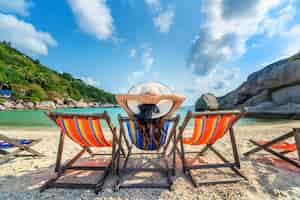 Free photo woman with hat sitting on chairs beach in beautiful tropical beach. woman relaxing on a tropical beach at koh nangyuan island