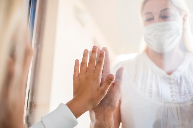 Free photo woman with medical mask in quarantine behind window with child