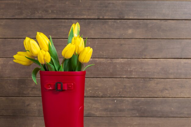 Wooden background with water boot and yellow tulips