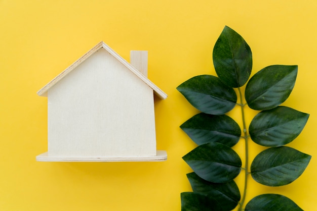 Free photo wooden house model near the green leaves against yellow background