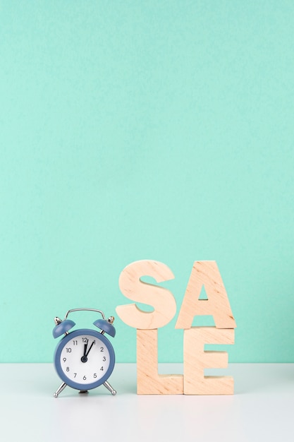 Free photo wooden sale lettering next to clock on blue background