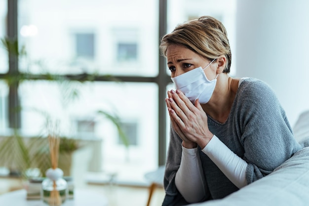 Foto gratuita donna preoccupata che prega con le mani giunte mentre indossa una maschera protettiva e si sente triste durante la pandemia di coronavirus