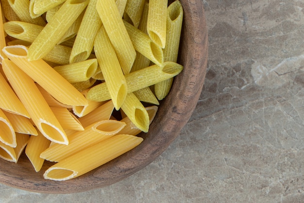 Free photo yellow and green penne pasta in wooden bowl.