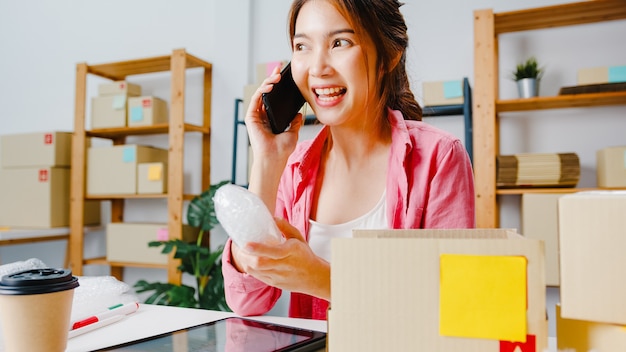 無料Photo 注文を受けた携帯電話を使用して若いアジア女性実業家と在庫の製品をチェック、ホームオフィスで働いています。中小企業のオーナー、オンライン市場の配信、ライフスタイルのフリーランスのコンセプト。