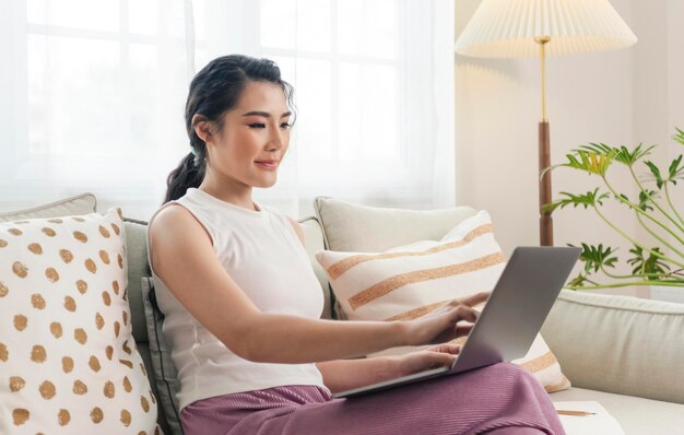 young asian businesswoman using laptop computer while relaxing on a couch at home work from home