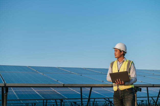 Free photo young asian inspector engineer man use laptop computer working at solar farm technician supervisor male in white helmet checking operation of sun and photovoltaic solar panel in station copy space