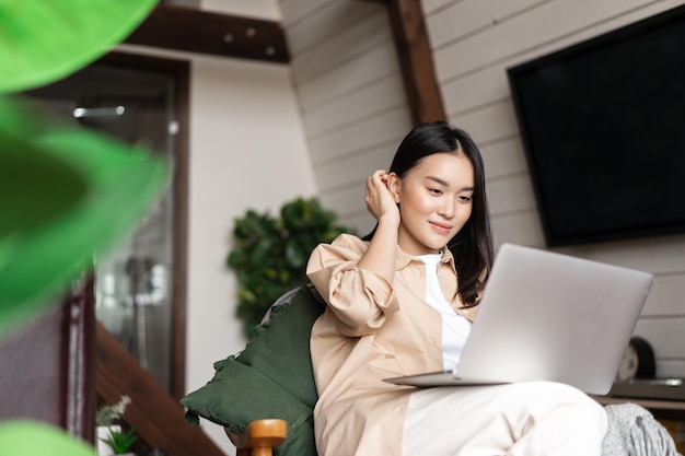 Бесплатное фото Молодая азиатская женщина, сидящая дома с девушкой портативного компьютера, просматривающая веб-сайты или обучающаяся удаленно